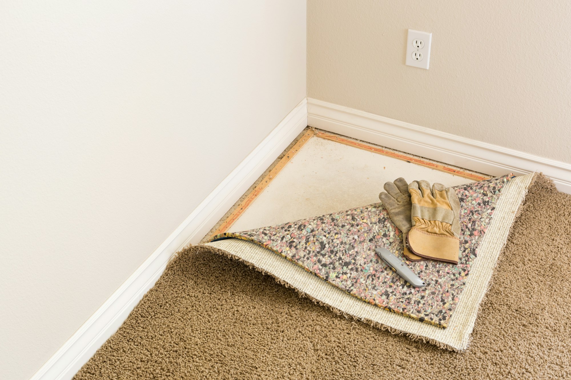 Gloves and Utility Knife On Pulled Back Carpet and Pad In Room.